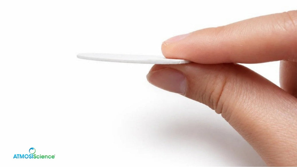 Hand holding a thin plant-fiber desiccant card edge-on against a white background