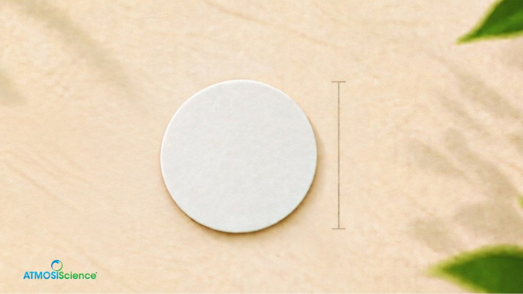 A round Fiber Desiccant Card on a sand-colored surface with green leaves